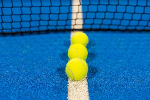 several balls by the net on a blue paddle tennis court. High quality photo