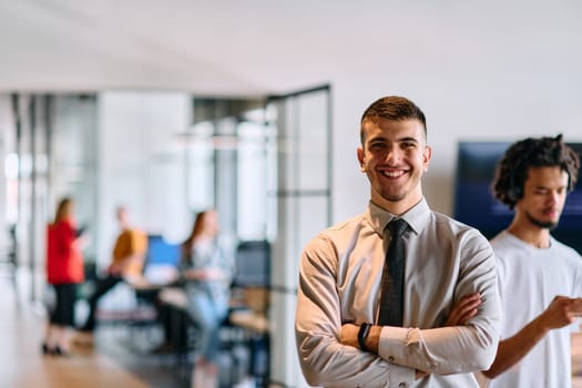 A young business leader stands with crossed arms in a modern office hallway, radiating confidence and a sense of purpose, embodying a dynamic and inspirational presence.