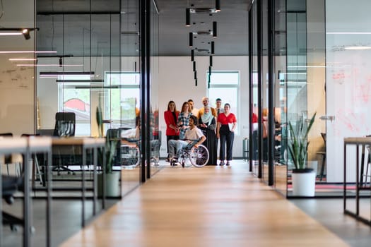 A diverse group of young business people walking a corridor in the glass-enclosed office of a modern startup, including a person in a wheelchair and a woman wearing a hijab.