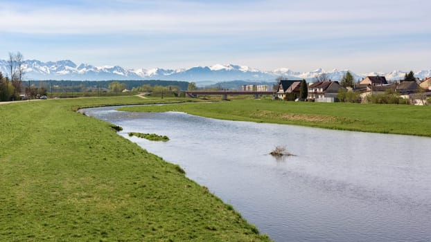 View of Bialy Dunajec river with residential buildings and Tatra mountains in the background in the city of Nowy Targ, Poland