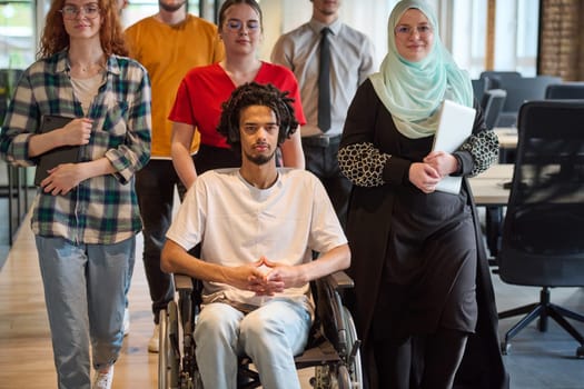 A diverse group of young business people congregates within a modern startup's glass-enclosed office, featuring inclusivity with a person in a wheelchair, an African American young man, and a hijab muslim woman