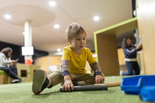 A young boy is sitting on the floor playing with a toy. The room is brightly lit and has a playful atmosphere