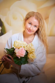 A blonde girl in a white terry bathrobe in hotel room with flowers. Wedding travel, Weekend and vacation, body care