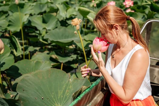 A woman is sitting in a boat in a field of pink lotus flowers