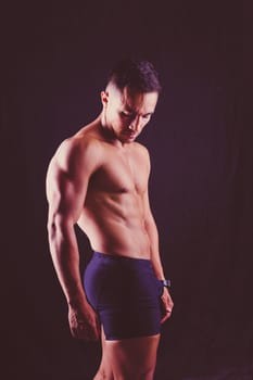 Confident, attractive shirtless muscular young man topless in a studio