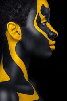Woman with black body paint. Cheerful young african girl with art bodypaint. An amazing model with yellow makeup. Closeup face.