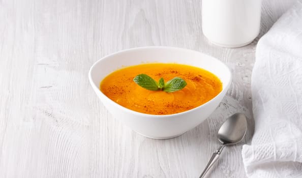 Pumpkin soup on a white wooden table, with copy space for text.