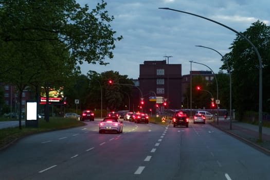 Hamburg, Germany - May 19, 2023: Vehicles are stopped at a red light during dusk, featuring a backdrop of illuminated city buildings and the onset of night.
