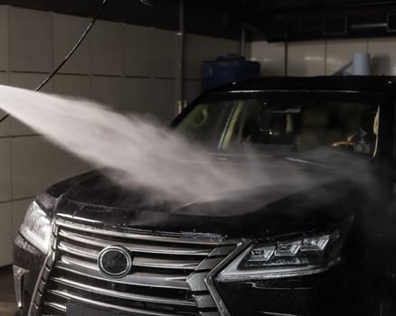 A man washes foam off a black car with water at a car wash