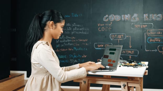 Highschool girl writing code or engineering prompt while attend in STEM technology class. Teenager coding or programing system while looking at computer screen in front of blackboard. Edification.