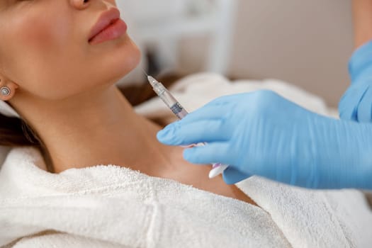 Closeup of young woman getting hyaluronic acid injections in chin at beauty salon. Cosmetology