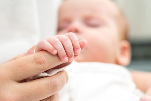 A resting newborn baby, illustrating absolute trust, securely holds onto the mother's reassuring finger