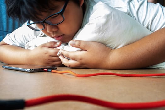 An Asian boy lies prone while seeing media on a smartphone