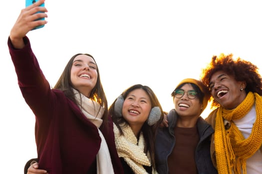 Happy multiracial group of smiling and cheerful college student friends taking selfie together in a sunny winter day using mobile phone. Copy space. Technology and lifestyle concept.