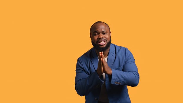 African american man putting hands together in begging gesture, making wish, isolated over yellow studio background. BIPOC person asking for something, praying and hoping, camera B