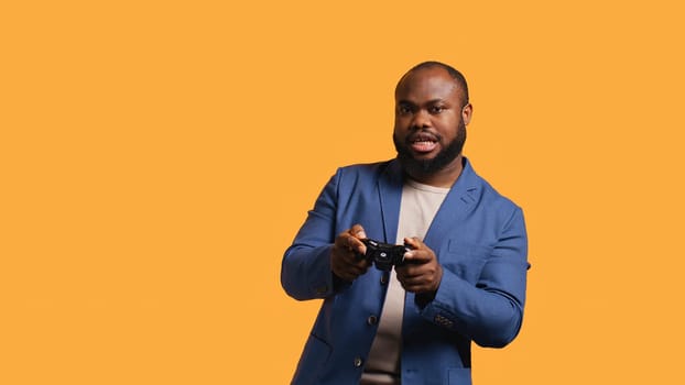 Upset man showing thumbs down sign gesturing holding controller, disapproving of videogames. Displeased BIPOC person against gaming, doing rejection hand gesture, studio background, camera B