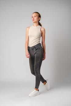 Girl in Beige Tank Top and Grey Jeans on gray background in studio