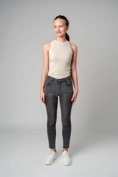 Girl in Beige Tank Top and Grey Jeans on gray background in studio