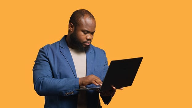 African american man using laptop to do business related tasks for company, isolated over studio background. Office clerk doing budgeting, forecasting, and financial analysis on notebook, camera A
