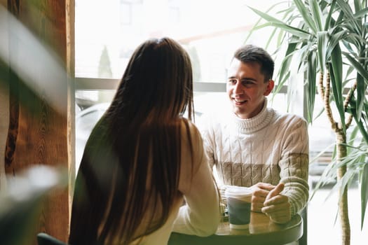 A man and woman are seated at a table engaging in conversation. They appear to be in deep discussion, leaning towards each other. The table is bare except for a few cups and plates. The man gestures with his hands while the woman listens intently.