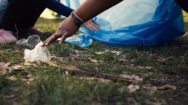 Diverse volunteers collecting trash and storing in the garbage bag, picking up junk and plastic waste to help with forest pollution. Clearing the woods, ecosystem protection. Close up. Camera B.