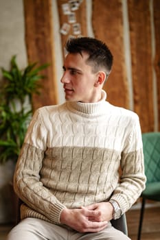 A man sitting comfortably in a chair, wearing a cozy sweater. He appears relaxed and content in a casual setting, with a warm ambiance.