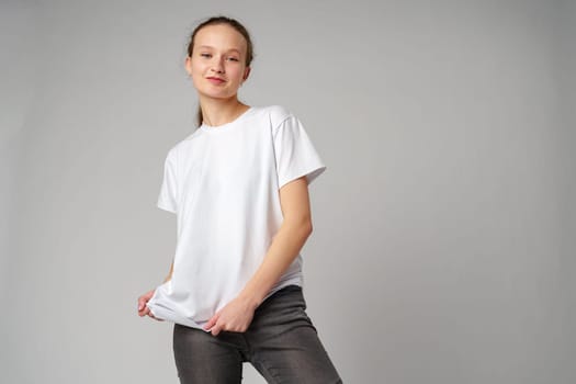 Beautiful young girl posing in white T-shirt and jeans on gray background in studio