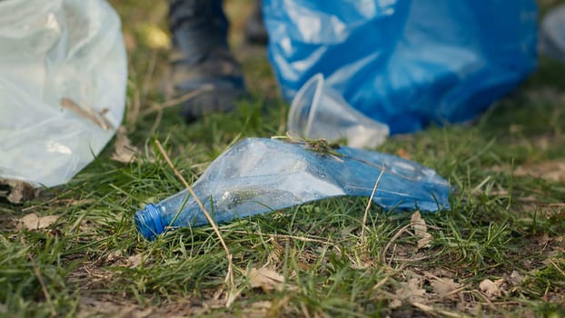 Group of volunteers cleaning the forest from litter and plastic waste, grabbing trash and junk with a long claw tool. Environmental activists picking up rubbish. Close up. Camera A.