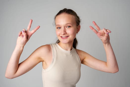 Young Girl Making a Peace Sign on gray background in studio