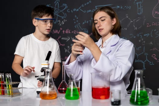 Teacher support schoolboy in laboratory. Schoolboy and teacher stand and experiment about science of chemistry in STEM class using liquid in glass container. Instructor mixing solution. Erudition.