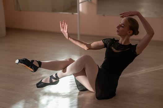 Woman in pointe shoes sits on the floor and does ballet warm-up