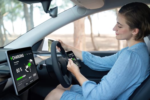 Holiday vacation road trip with environmental-friendly car concept. Eco-conscious woman on driver seat checking EV car's battery status display on tablet or car panel during car travel. Perpetual