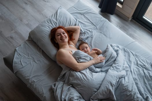 Top view of a red-haired Caucasian woman lying in bed with her baby son