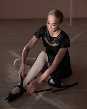 Woman sitting on the floor and tying ribbons on her pointe shoes. Vertical photo