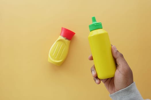 holding a bottle of mustard mayonnaise on yellow background .
