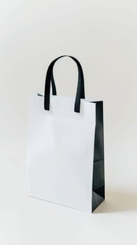 A white bag with black handles is placed on a plain white background. The bag stands out with its contrasting colors, creating a simple and elegant composition.