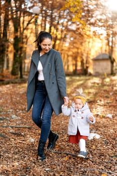 Mom and a little girl are walking, holding hands, through the autumn sunny forest. High quality photo