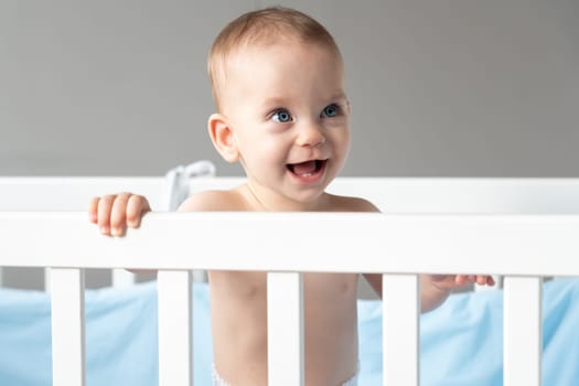 A baby laughing out loud looks out of a crib with interest.