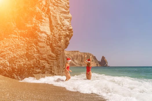 Women Santa hats ocean play. Seaside, beach daytime, enjoying beach fun. Two women in red swimsuits and Santa hats are enjoying themselves in the ocean waves and raising their hands up