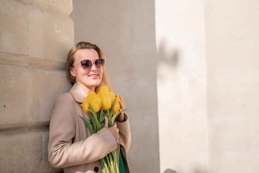 Woman holding yellow tulips, leaning against stone wall. Women's holiday concept, giving flowers