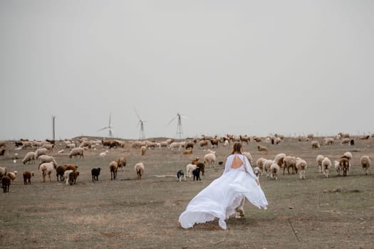 A woman in a white dress is walking through a field of cows. The cows are scattered throughout the field, with some closer to the woman and others further away. The scene has a peaceful