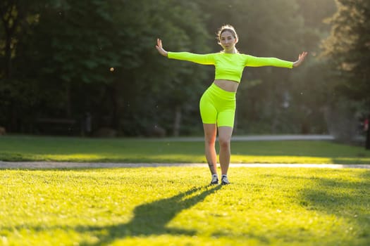 A woman in neon green is standing in a field of grass. She is wearing a neon green top and shorts