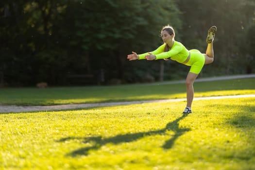 A woman in a neon yellow outfit is doing a yoga pose on a grassy field. The bright colors of her outfit and the green grass create a cheerful and energetic mood. Concept of health and wellness