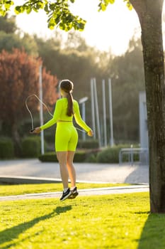 A woman in a neon yellow outfit is jumping rope in a park. The scene is bright and cheerful, with the sun shining down on the grass and the woman's outfit adding a pop of color to the scene