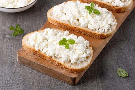 Bread with curd cheese on grey wooden table.