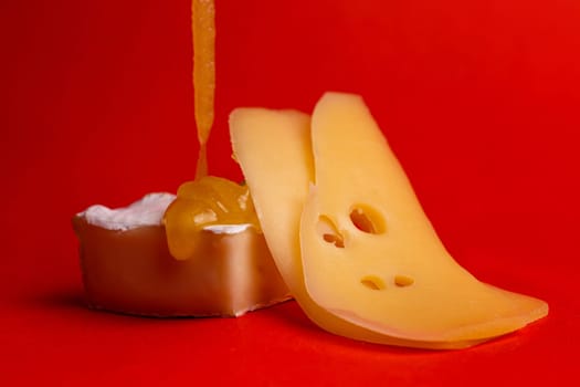 hard and soft cheese with honey on a red background.