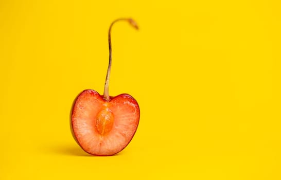 ripe cherry with a stone in a section on a yellow background.