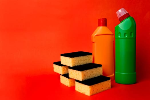 two bottles of cleaning products and cleaning sponges on a red background.