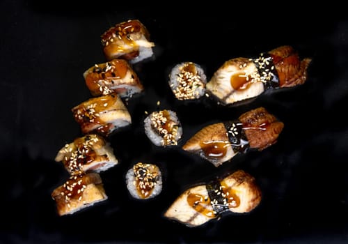 baked rolls and sushi on a black background top view