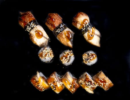 baked rolls and sushi on a black background top view.